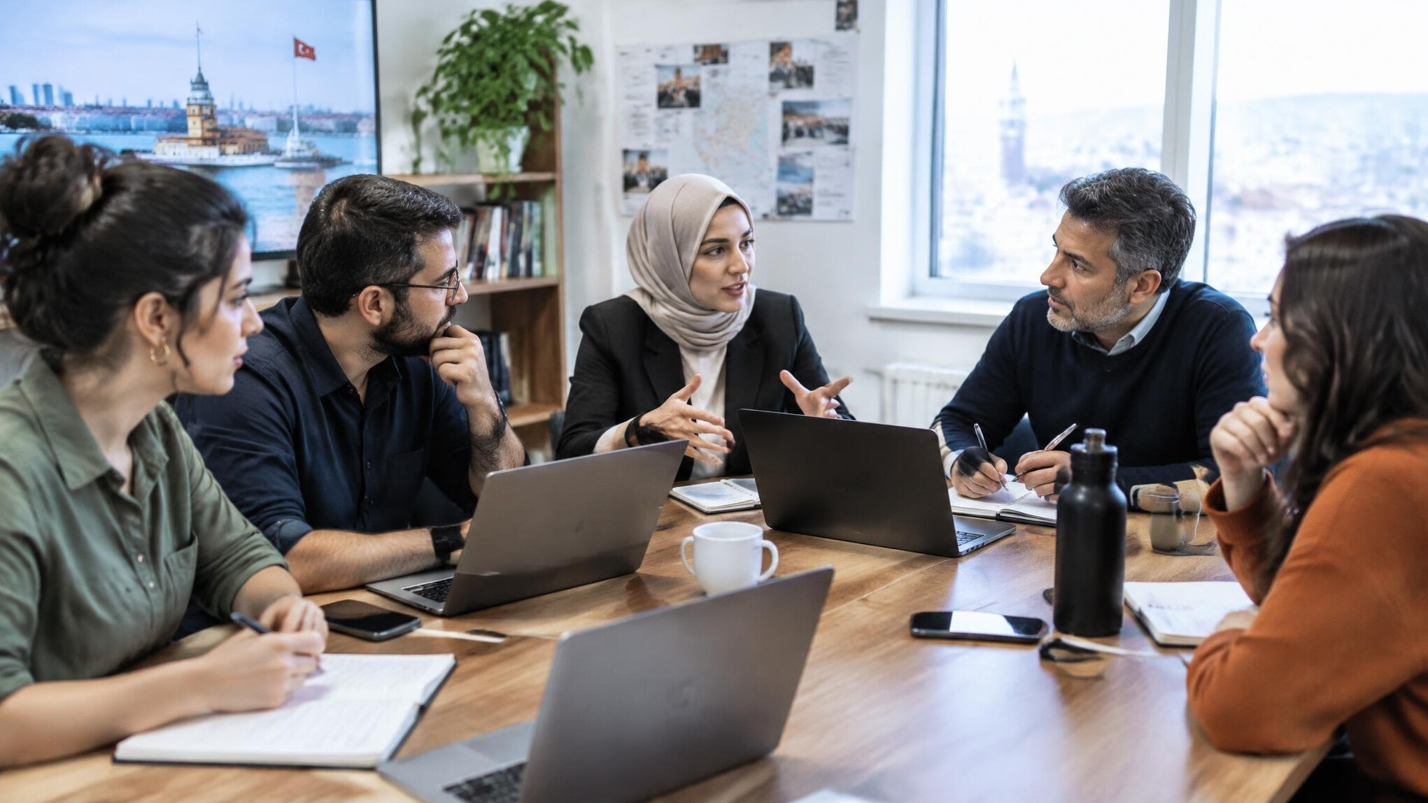 Editorial team meeting around a table with laptops